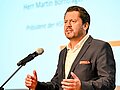 Martin Bornträger steht an einem Rednerpult. Hinter ihm ist eine Videoleinwand zu sehen.