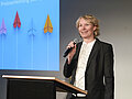 Lehrpreis 2025 Stefanie Haumer am Rednerpult vor einer Beamerprojektion. In der rechten Hand hält sie ein Mikrofon.