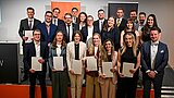 Die Graduierten stehen auf einer Bühne. Hinter ihnen ist das Logo der HSPV NRW zu sehen.